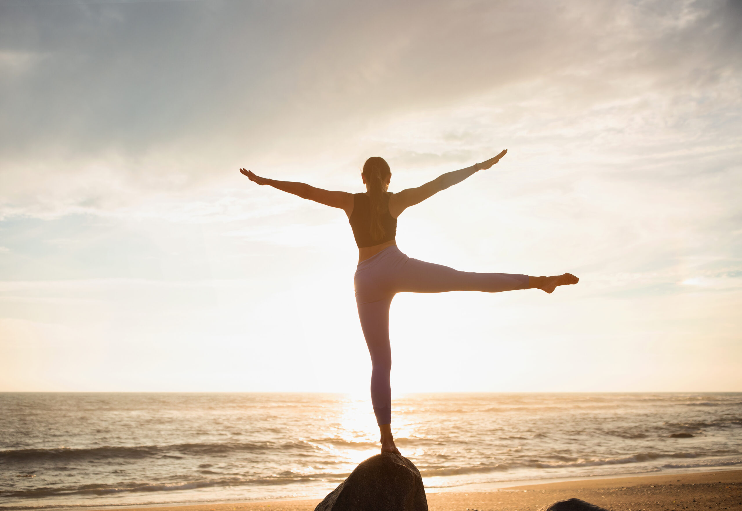 Young caucasian woman professional athlete practice yoga, enjoy breathing exercises, balance on stone on sea beach. Morning workout, sports alone, health care and active lifestyle